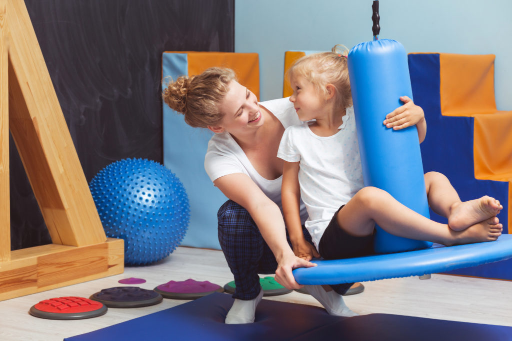Sensory integration in training Young physiotherapist seesawing the girl on a blue swing