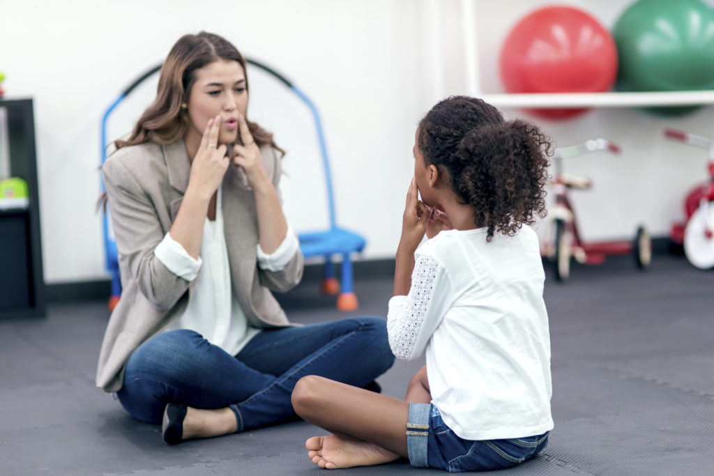Adult female therapist guiding young girl in speech therapy for a therapy exercise